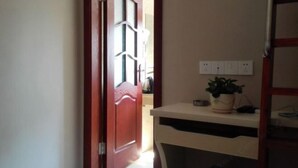 A hallway with a red door, a white wall with electrical outlets, and a small table with a potted plant. - Buding Inn (Yi County)