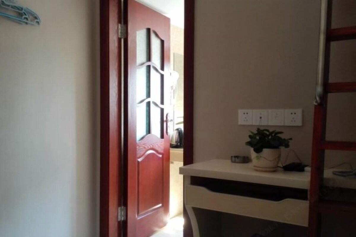 A hallway with a red door, a white wall with electrical outlets, and a small table with a potted plant.