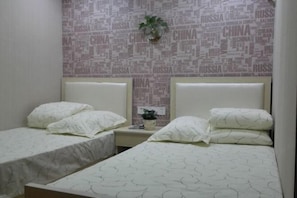 A hotel room with two single beds, a small bedside table with a plant, and a wall with a word cloud design. - Buding Inn (Yi County)