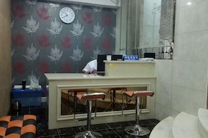 A reception area with a desk, a clock, and a patterned wall. - Buding Inn (Yi County)