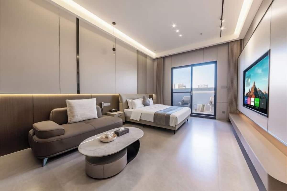A modern hotel room with a sofa, a bed, a TV, and a large window.