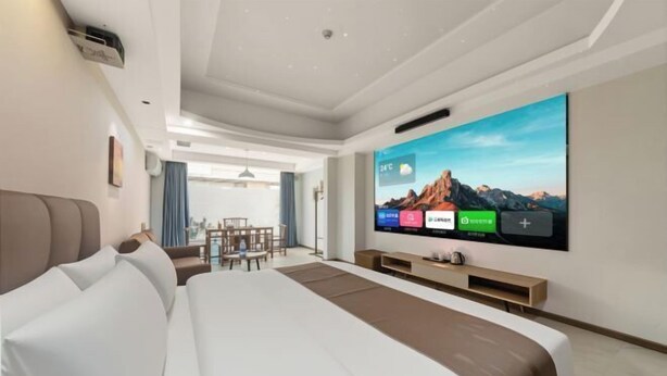 Ein modernes Hotelzimmer mit einem großen Bett, einem wandmontierten Flachbildfernseher und einem Essbereich, der durch eine offene Tür sichtbar ist.