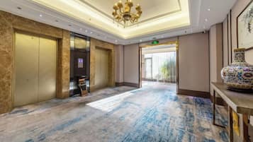 A hotel lobby with a marble floor, elevator, reception desk, and a large vase.