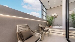 Ein moderner Sitzbereich im Freien mit Korbstühlen und einem kleinen Tisch, einem großen Spiegel an der Wand und Blick zum Himmel.