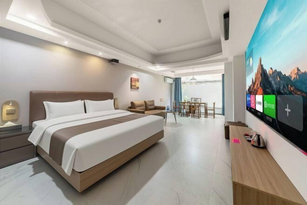 A modern hotel room with a large bed, a desk, and a TV mounted on the wall.