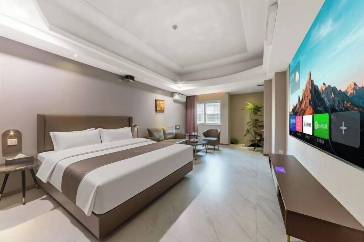 A modern hotel room with a large bed, a desk, a chair, a TV, and a painting on the wall.