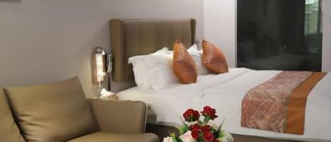 Una habitación de hotel con cama, sofá, un jarrón de flores y una mesita de noche.