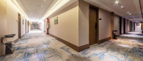 Un couloir d’hôtel avec un sol recouvert de moquette, des portes de chaque côté et un éclairage au plafond.