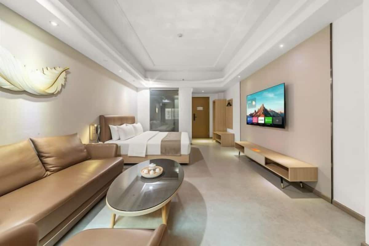 A modern hotel room with a sofa, a bed, a TV, and a coffee table.