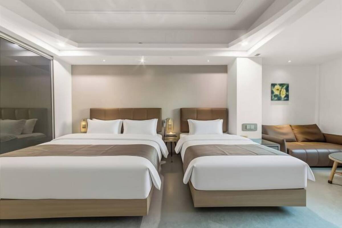 A modern hotel room with two beds, a sofa, a small table, and a painting on the wall.