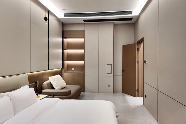 A modern hotel room with a large bed, a seating area, and built-in storage cabinets. - Meiting Garden Apartment (Shantou)