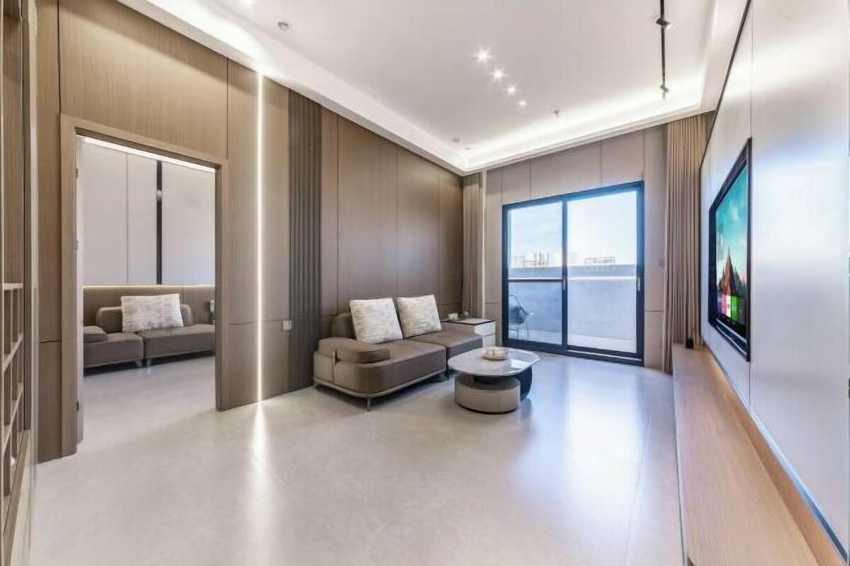 A modern living room with a sofa, coffee table, and a large window offering a city view.