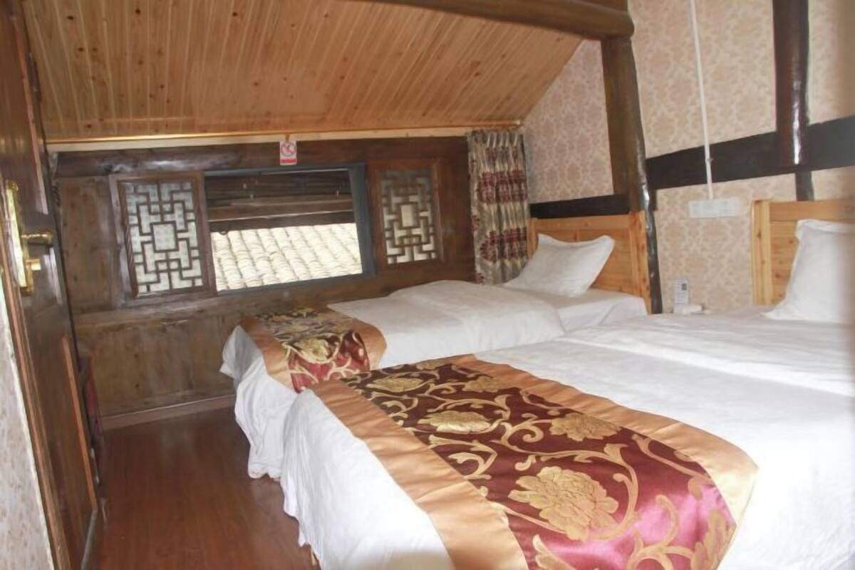 A room with two beds, wooden ceiling beams, and a window with patterned shutters.