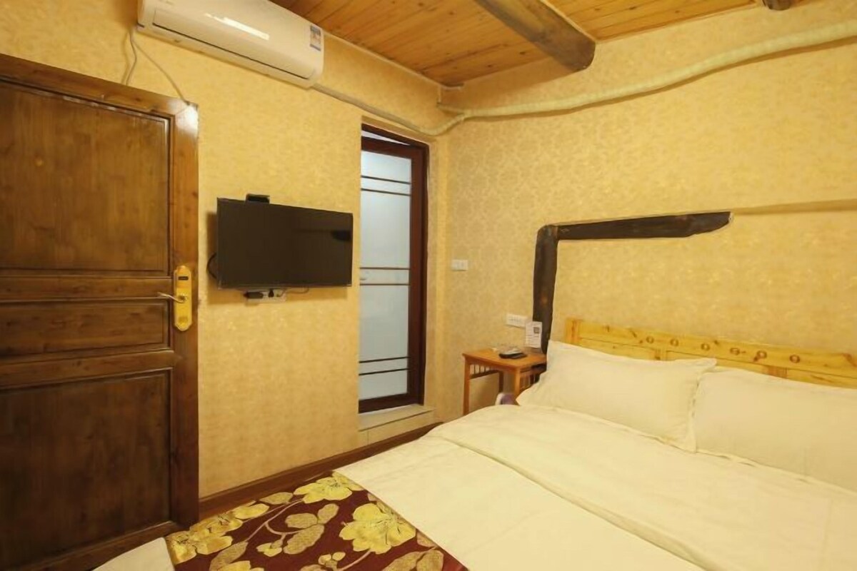 A hotel room with a wooden door, a bed with white linens, a small bedside table, and a television mounted on the wall.
