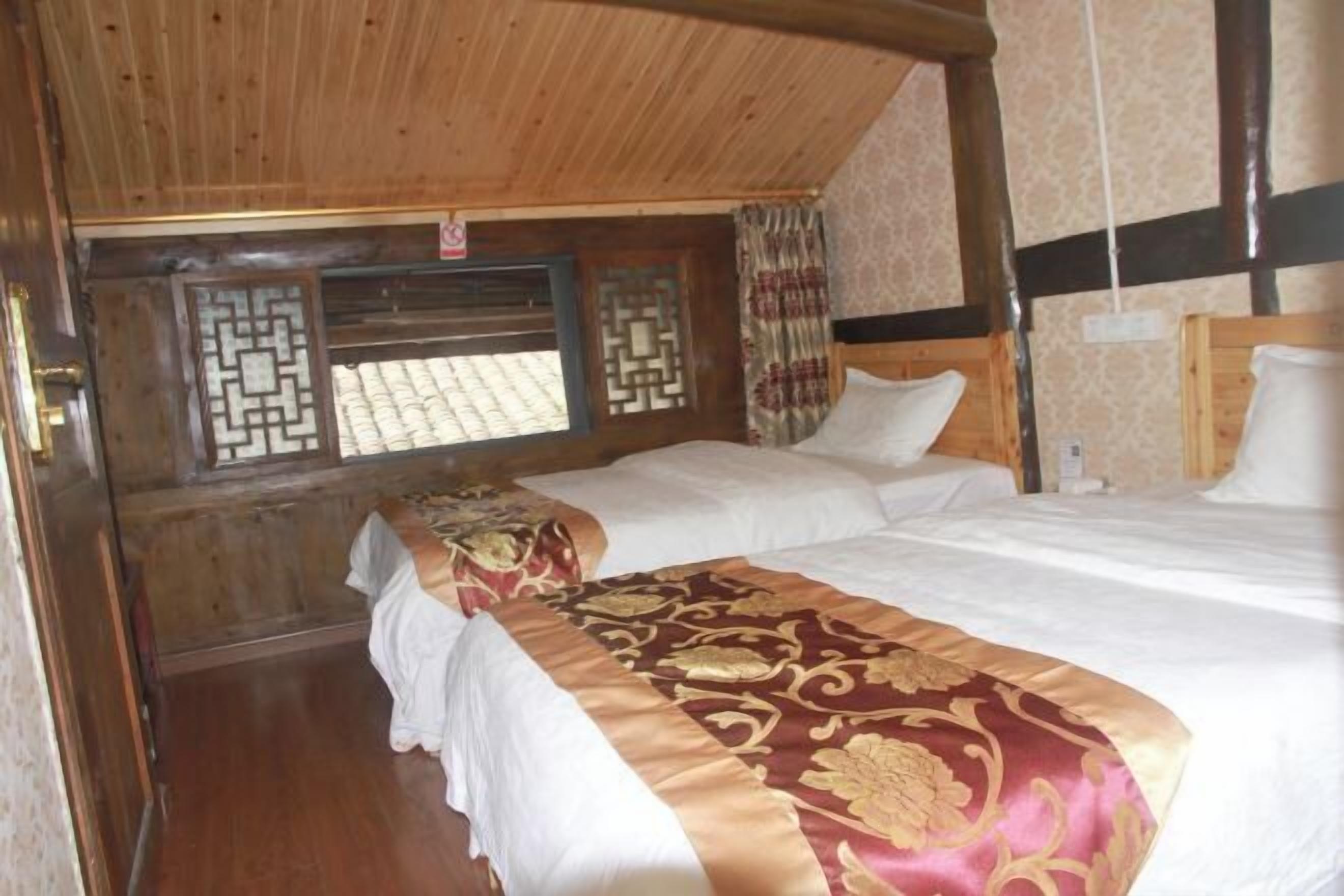 A room with two beds, wooden ceiling beams, patterned window shutters, and a wooden door.