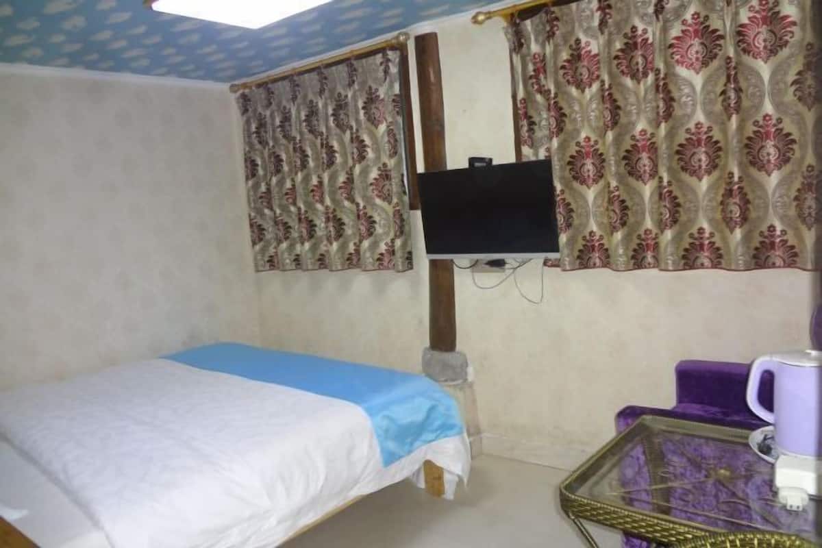A room with a bed, a television mounted on the wall, and a small table with a purple chair.