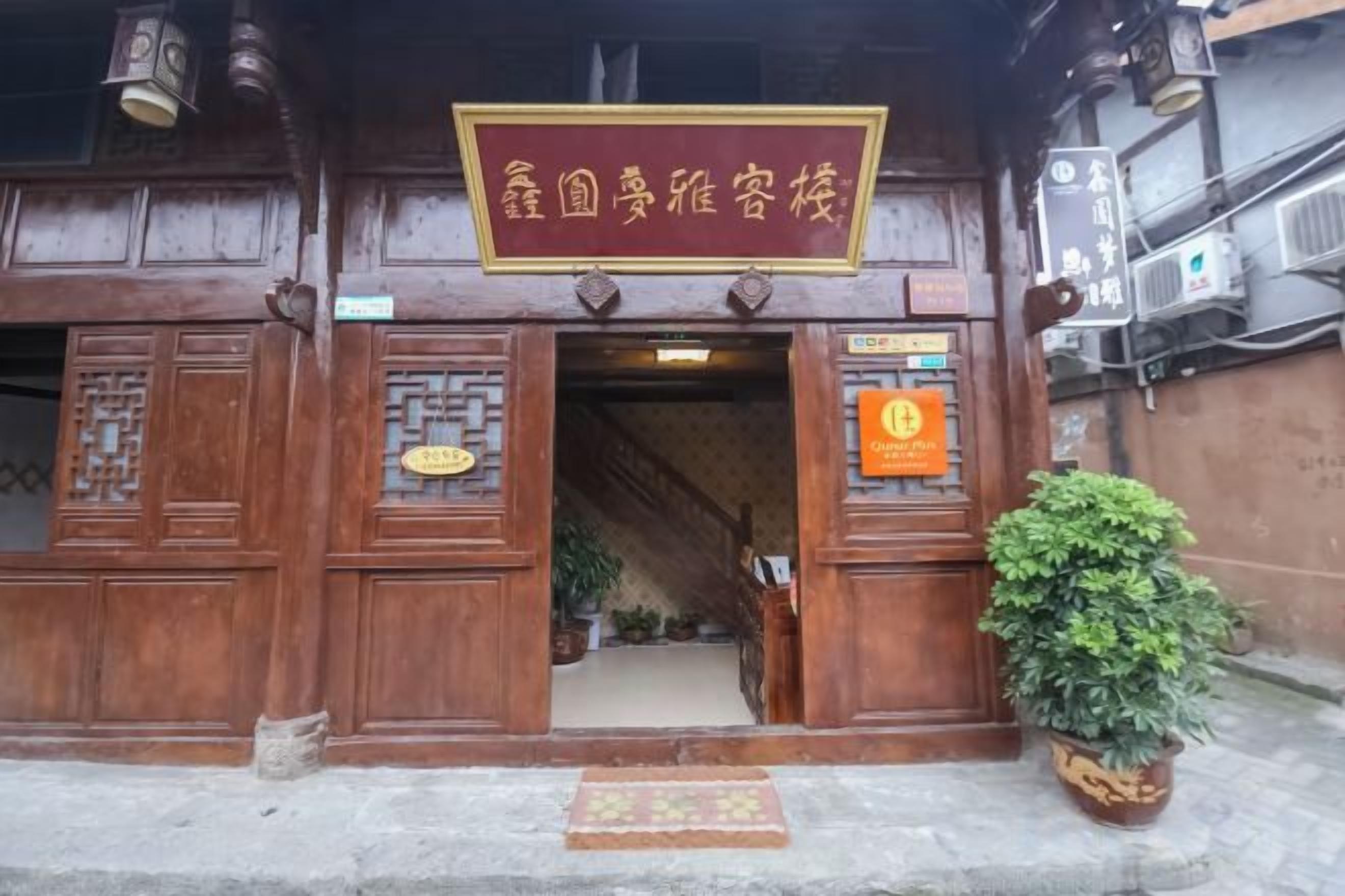 A traditional wooden building with a signboard, a staircase leading inside, and a potted plant on the ground.