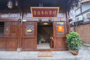 A traditional wooden building with a signboard, a staircase leading inside, and a potted plant on the ground. - Xinyuan Mengya Inn (Langzhong)