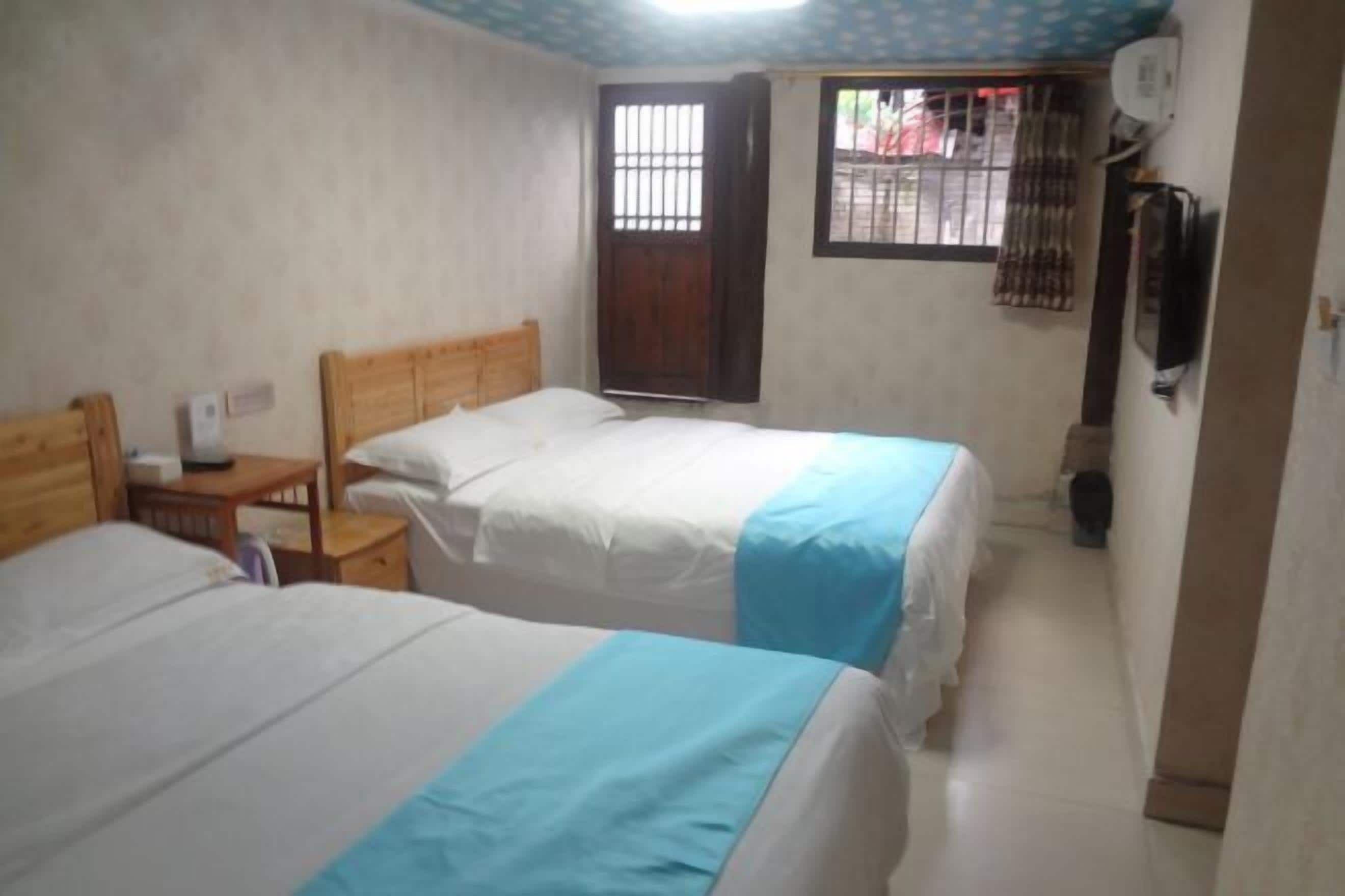 Habitación con dos camas, una mesita de noche de madera, una pequeña mesa, una ventana con rejas y un televisor montado en la pared.