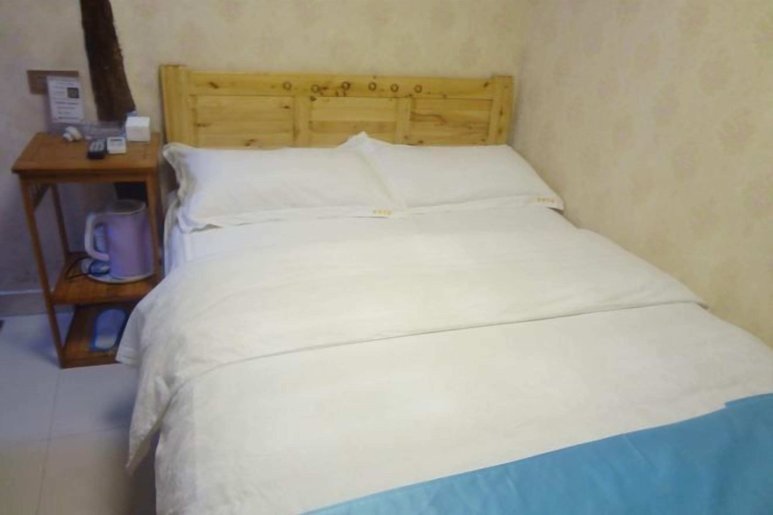 A single bed with a wooden headboard, a nightstand with a lamp, and a wall-mounted telephone.