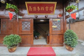 A traditional wooden entrance with a red mat, potted plants, and a sign with Chinese characters. - Xinyuan Mengya Inn (Langzhong)