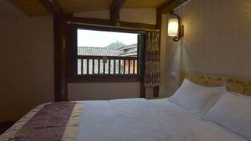Quarto com cama, janela com vista para edifícios e luminária fixada na parede.