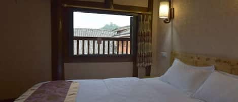 A bedroom with a bed, a window with a view of buildings, and a wall-mounted light fixture.