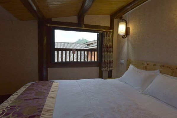A bedroom with a bed, a window with a view of buildings, and a wall-mounted light fixture. - Xinyuan Mengya Inn (Langzhong)