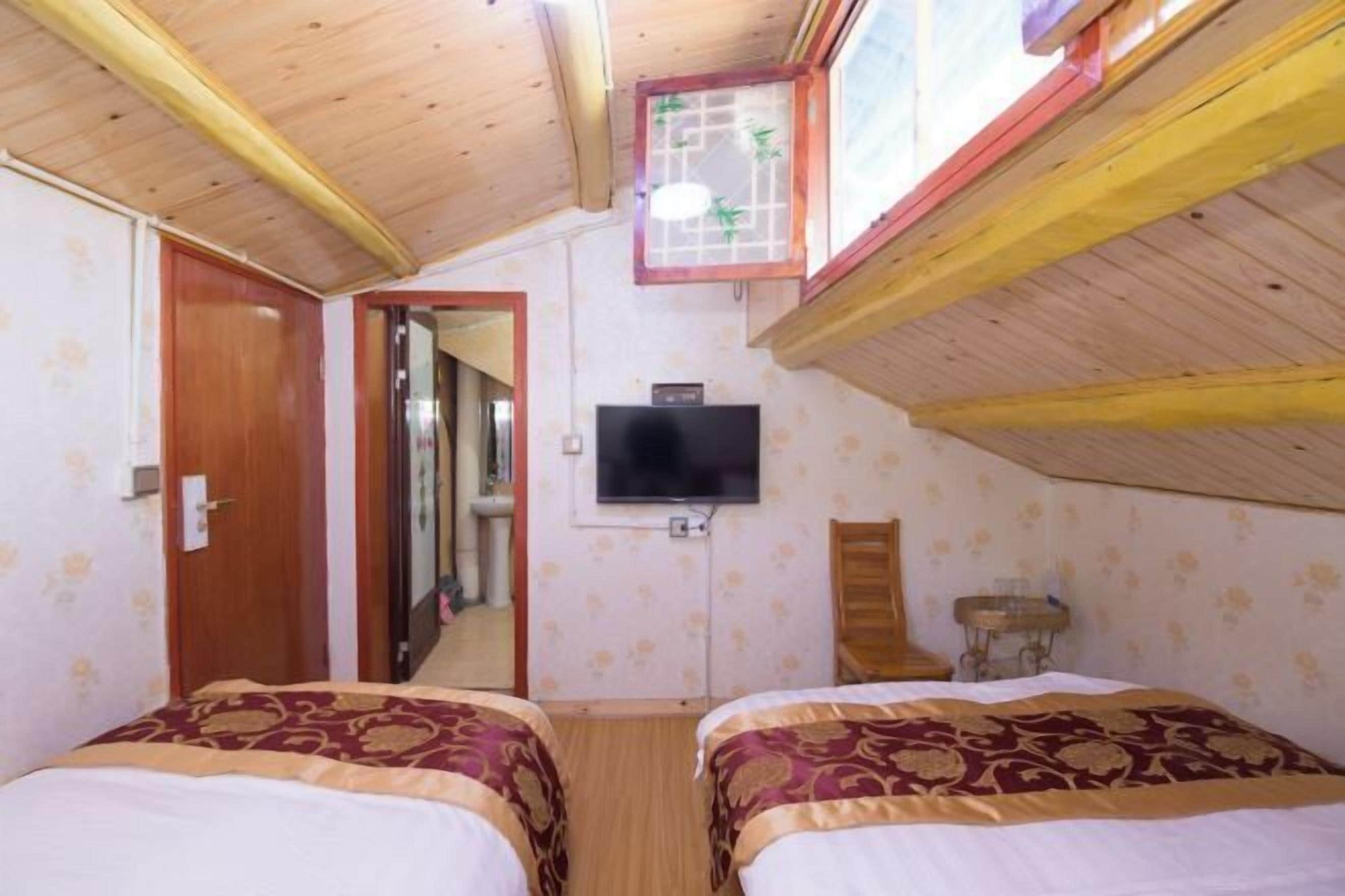 A bedroom with two beds, a TV, and a wooden ceiling.