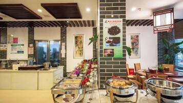 Un área de bufé con varias estaciones de comida, un refrigerador y una zona de estar con mesas y sillas.