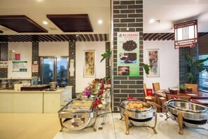 A buffet area with multiple food stations, a refrigerator, and a seating area with tables and chairs. - Landu Business Hotel (Tengchong)