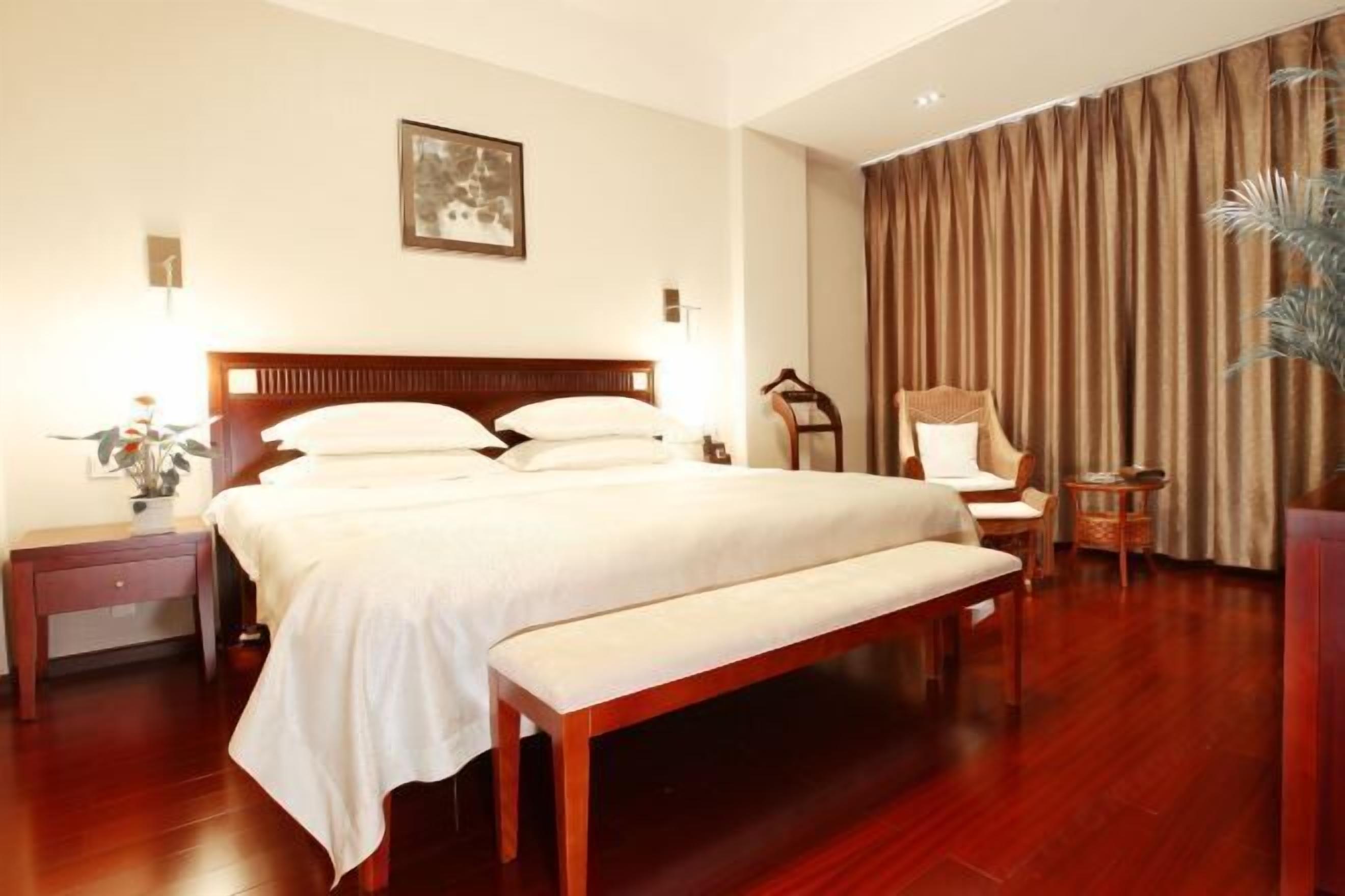 A hotel room with a large bed, bedside tables, a chair, a small table, and a curtain.