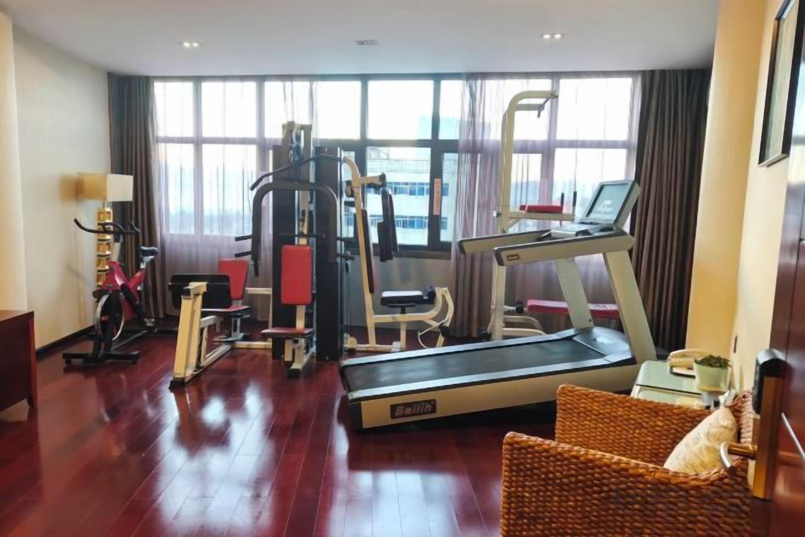 A hotel room with a treadmill, exercise equipment, and a large window with curtains.