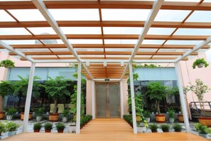 A covered walkway with a wooden floor, flanked by potted plants and a glass door at the end. - Landu Business Hotel (Tengchong)