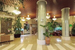 Vestíbulo con techo alto, columnas grandes y plantas colgantes.