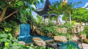 A traditional pavilion surrounded by lush greenery and a small waterfall. - Landu Business Hotel (Tengchong)