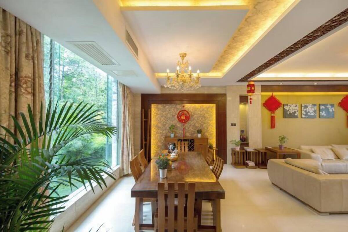 A dining area with a wooden table and chairs, a chandelier, and a sofa in a modern living room.