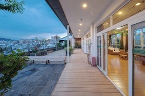 A hotel corridor with a wooden floor, glass doors leading to a seating area, and a view of the cityscape. - Landu Business Hotel (Tengchong)