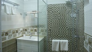 A modern bathroom with a glass-enclosed shower, a white sink, and decorative mosaic tiles.