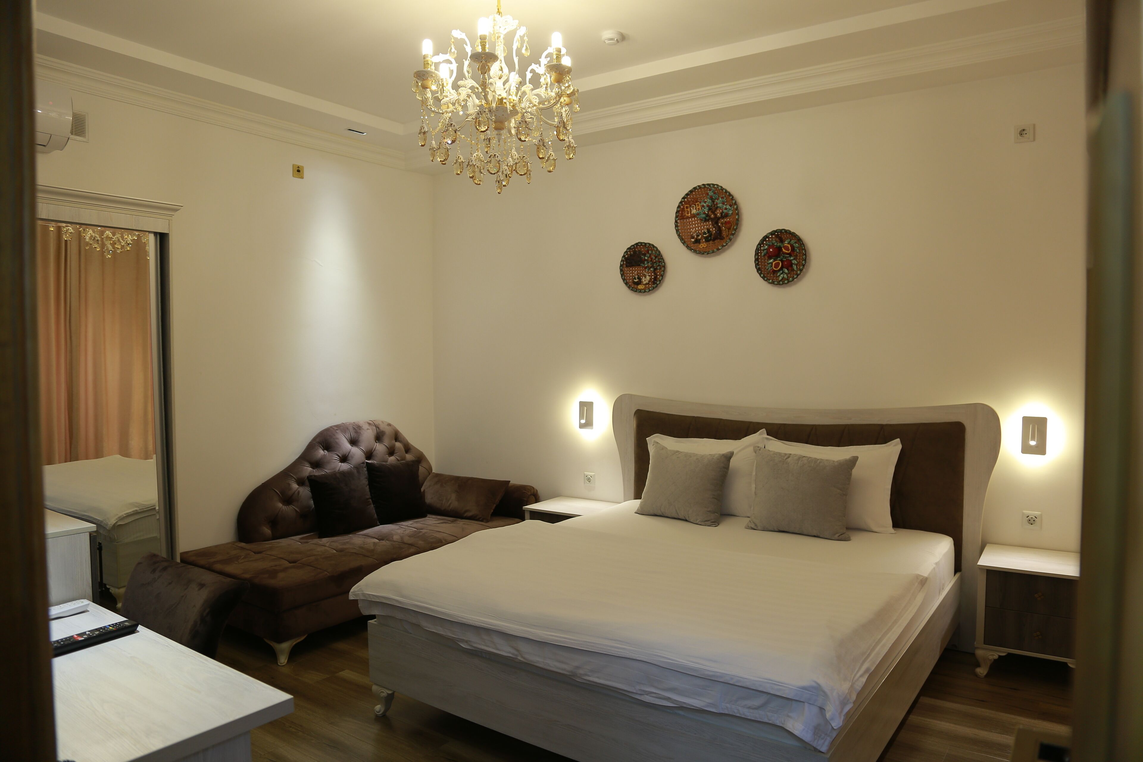 A bedroom with a large bed, a chaise lounge, a desk, and a chandelier.