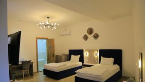 A hotel room with two beds, a desk, a chair, a television, and a chandelier.