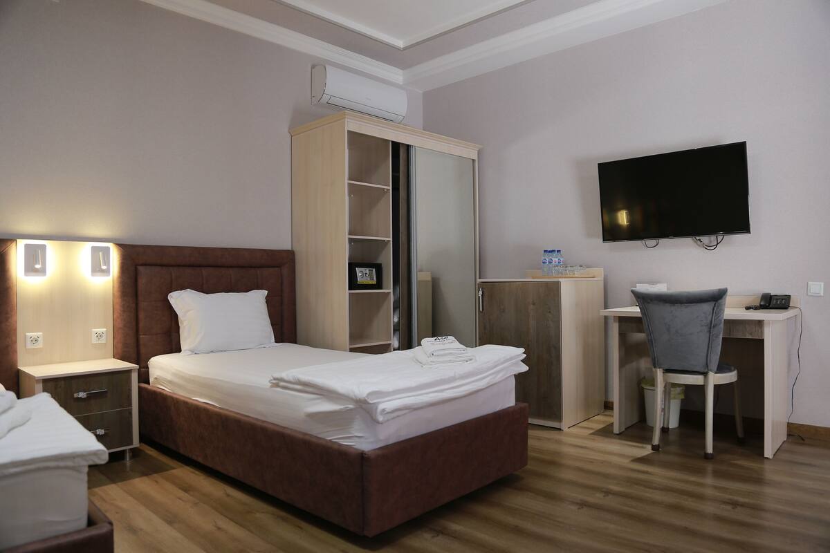 Une chambre d’hôtel comprenant un lit, une armoire, un bureau, une chaise, une télévision et une table de chevet avec une lampe.