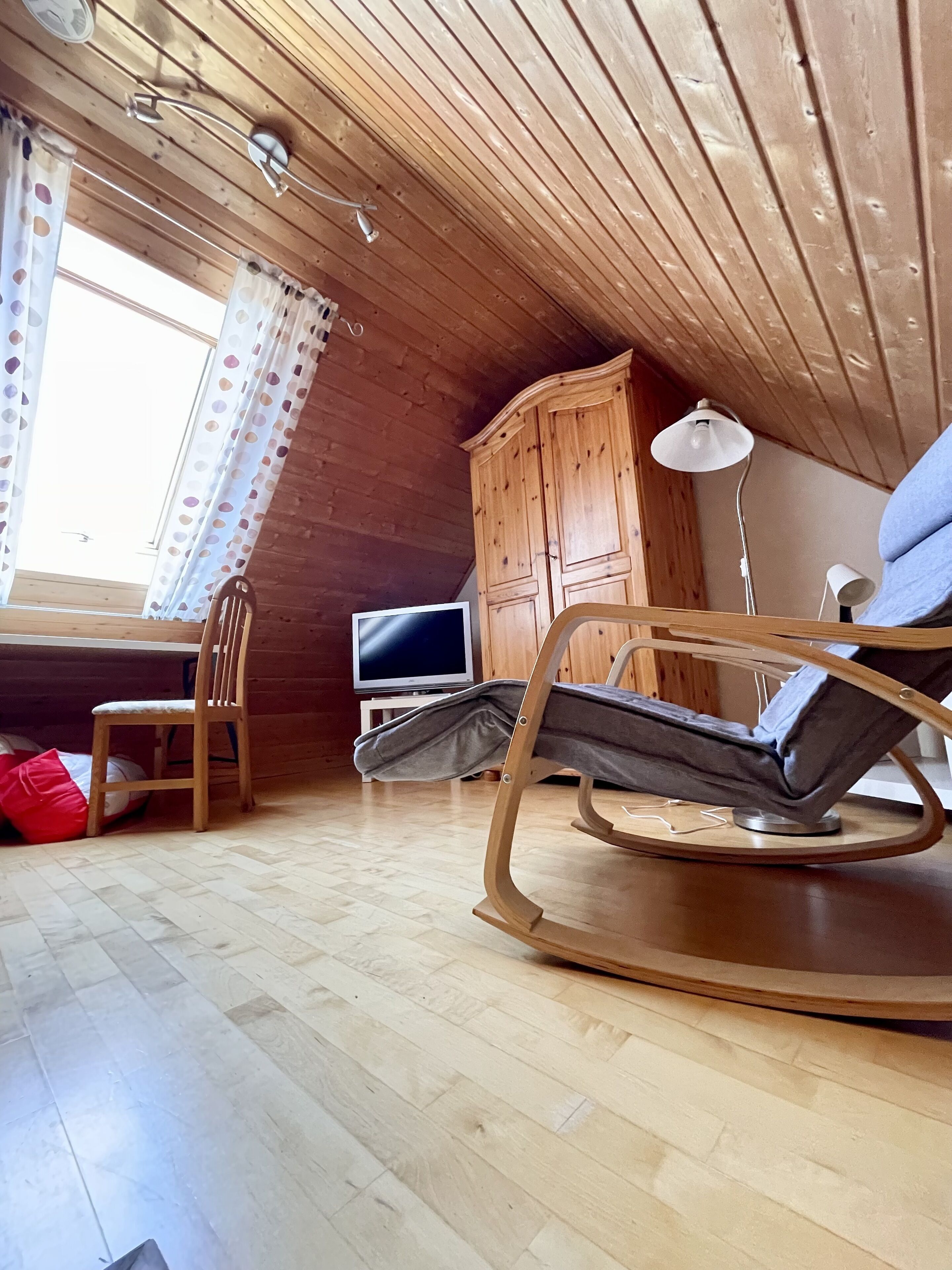 Una habitación acogedora de madera con una mecedora, un televisor y un armario.