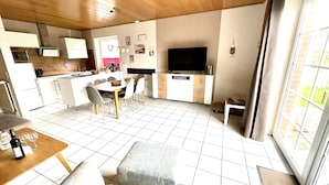 A modern kitchen with a dining area, a TV, and a large window. - Ferienhaus in Nessmersiel, Deich- und Inselblick, Glasfaser (Dornum)
