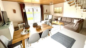 A modern living room with a dining area, a sofa, and a TV. - Ferienhaus in Nessmersiel, Deich- und Inselblick, Glasfaser (Dornum)