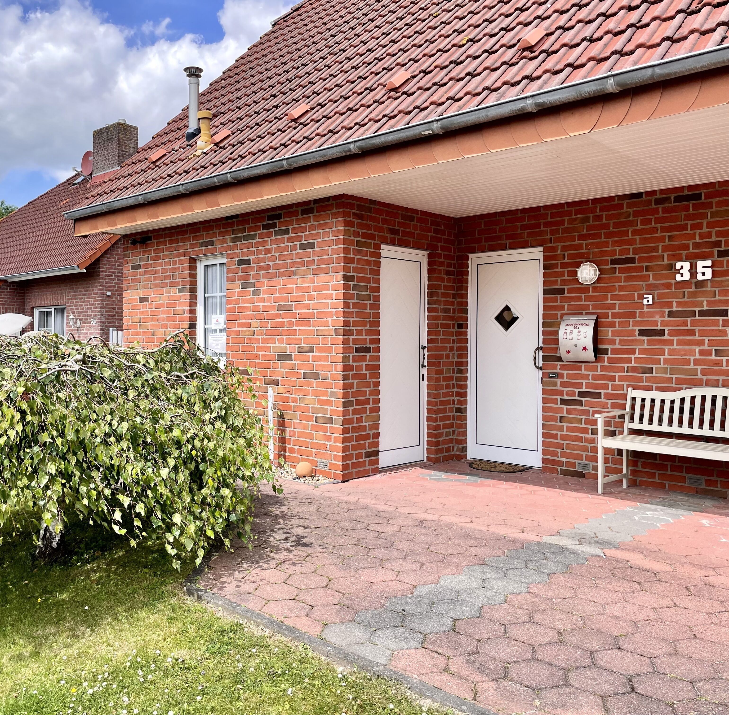 A brick building with a red-tiled roof, two white doors, and a bench outside.