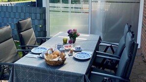 An outdoor patio with a table set for breakfast, including bread, eggs, and flowers. - Ferienhaus in Nessmersiel, Deich- und Inselblick, Glasfaser (Dornum)