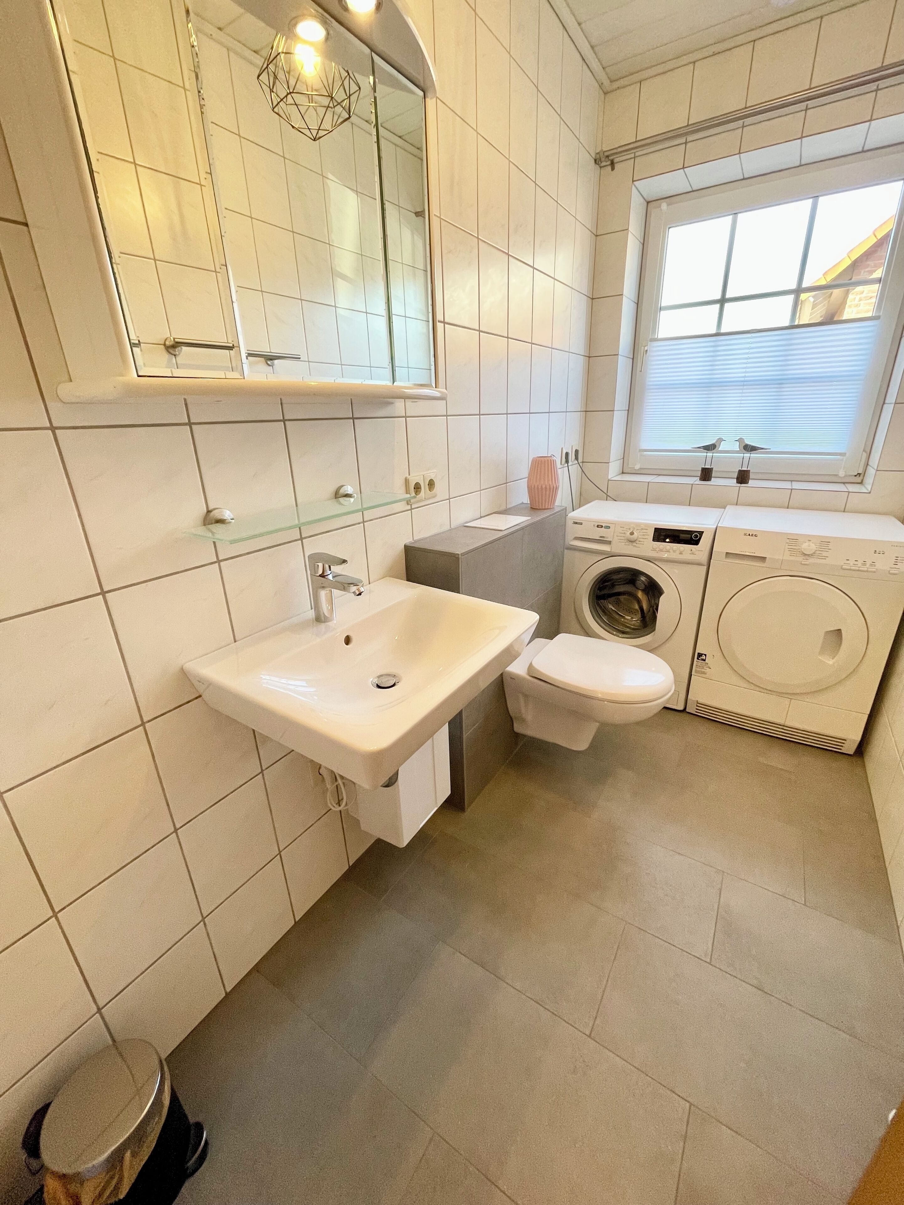 Une salle de bain moderne avec un lavabo blanc, des toilettes et un lave-linge encastré.