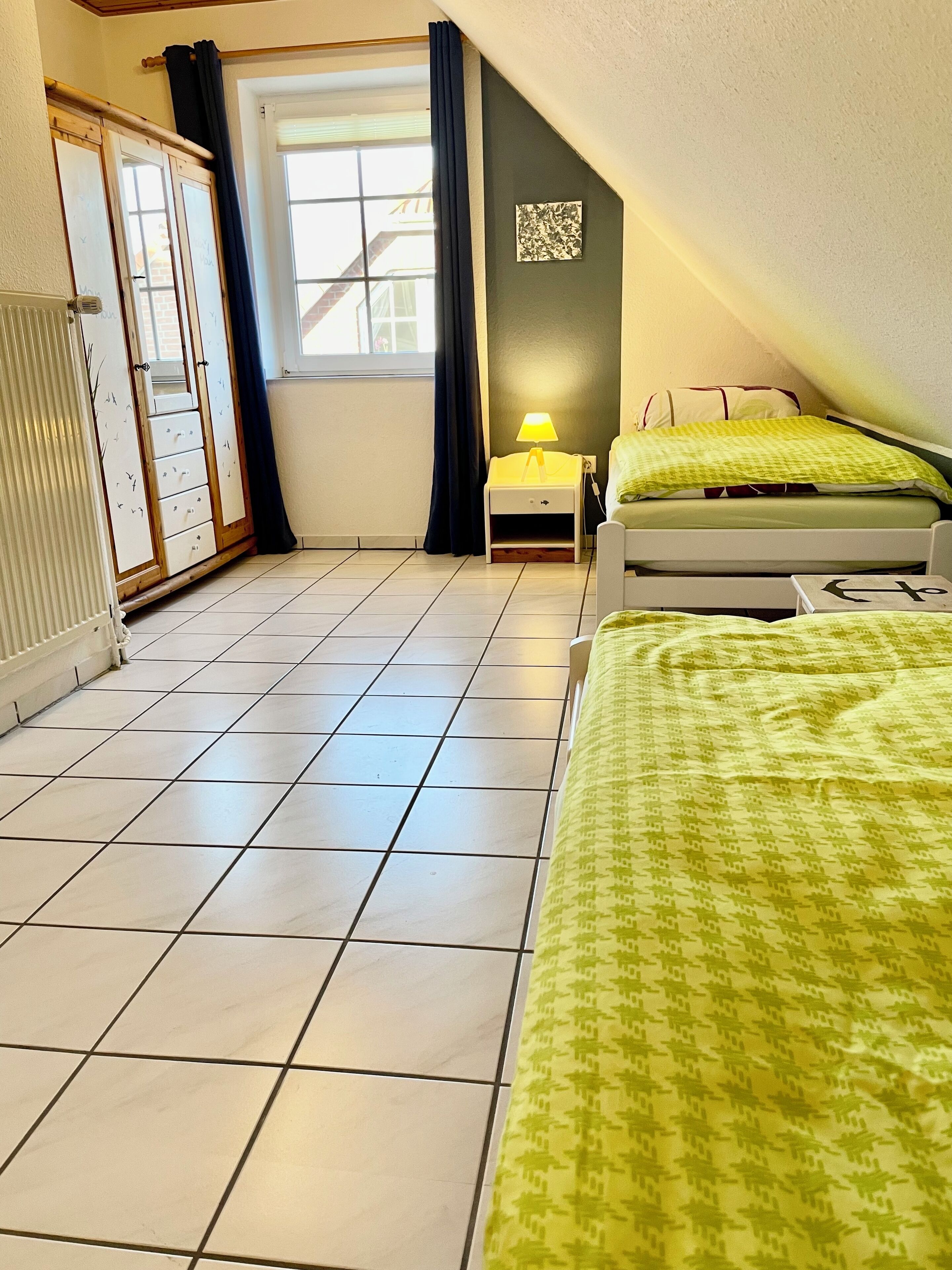 Un dormitorio con cama, mesita de noche, lámpara y ventana con cortinas.