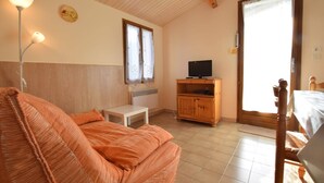 Une pièce chaleureuse avec un plafond en bois, un canapé, une petite table, un téléviseur posé sur un meuble en bois et une porte-fenêtre coulissante.